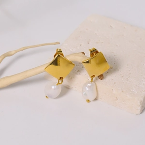 Elegant geometric gold square studs with dangling baroque pearls on a stone background