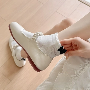Close-up of white Mary Jane shoes and lace ruffle socks with black bows on wooden floor