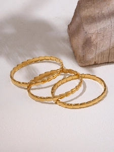 Close-up of three 18K gold-plated geometric link bracelets on a minimalist stone background