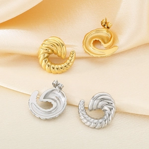 Macro detail of gold and silver spiral textured croissant stud earrings on silk cloth