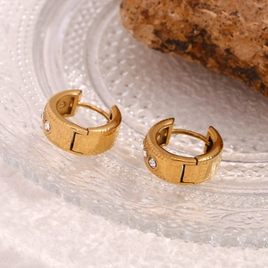 Macro shot of gold plated twist hoop earrings with inlaid zircons on a glass tray
