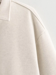 Close-up of the cream wool coat showing the minimalist collar and premium fabric texture