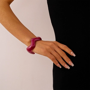 Close-up of a wavy fuchsia acrylic resin bangle with marble texture on a black sleeve