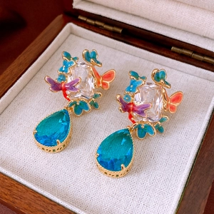 Macro shot of gold plated earrings featuring butterfly enamel and zircon drop pendant