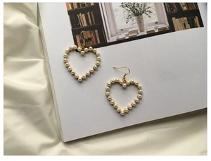 Close-up of elegant heart-shaped pearl drop earrings with golden hooks on silk fabric