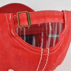 Detail of red baseball cap showing metal adjustable buckle and white stitching textures