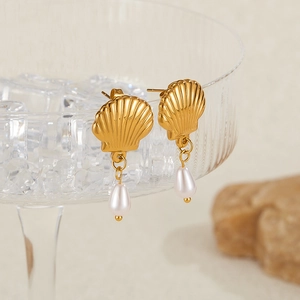 Detail of gold shell earrings with teardrop pearl on textured glass container