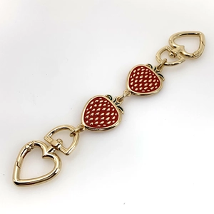 Golden strawberry extender chain with red enamel charms for handbags on white background