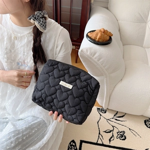 Detail of black heart quilted makeup bag with gold logo patch and zipper closure