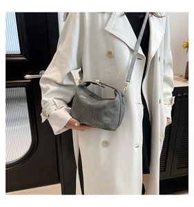 Detail view of a grey suede-textured pillow bag worn with a white trench coat