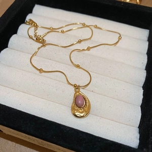 Close-up of gold chain necklace with pink oval gemstone pendant in a jewelry box