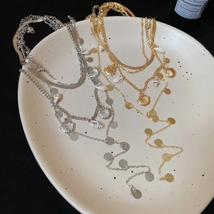 Detail of layered gold and silver necklaces with shell pendants and sequins on a plate