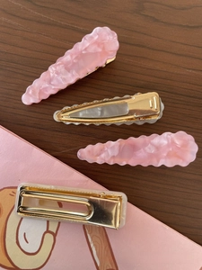 Detail of pink marble resin hair clips set with golden metal base on a wooden desk