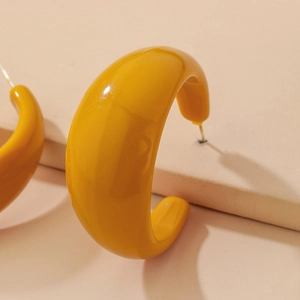 Detailed close-up of glossy yellow C-shaped acrylic hoop earrings with silver pins