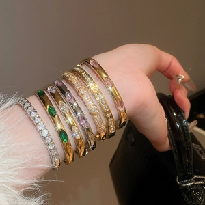 Close-up of stacked gold-plated bracelets featuring heart-shaped colorful zircons on a hand