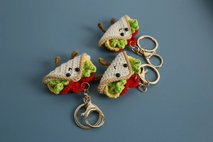 Macro detail of three handmade crochet taco keychains with cute faces and gold hardware