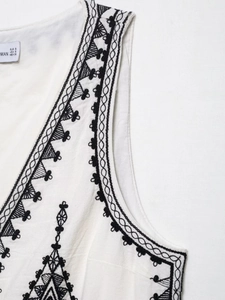 Detailed close-up of ethnic embroidery on white vest with size tag and stitch texture