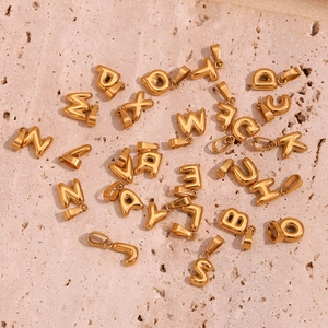 Detail of puffy 18K gold plated stainless steel letter pendants on a stone surface
