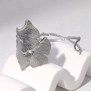 Macro detail of silver ginkgo leaf stainless steel bangle with fine texture on white stand