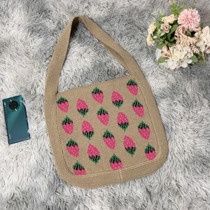 Close-up of khaki knitted tote bag featuring a pink strawberry pattern on faux fur rug
