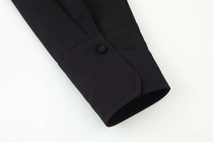 Close-up of black sleeve cuff featuring a fabric-covered button and fine plain weave texture