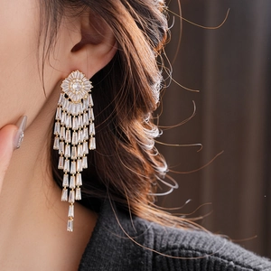 Close-up of gold-plated tassel earrings with rectangular crystals worn by a model