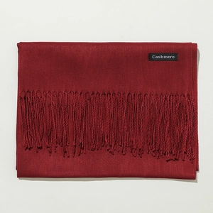 Detail shot of a red cashmere scarf featuring soft tassels and a woven material label