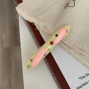 Detail of a beige acrylic hair clip with pink 3D accents and colorful sparkling rhinestones
