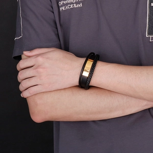 Close-up of men's triple-layer braided leather bracelet with golden engraved metal plate