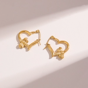 Minimalist gold stainless steel heart earrings with small bee charm on a textured surface
