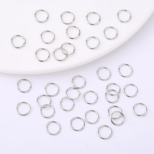 Detailed view of silver open jump rings scattered on a white porcelain surface for DIY jewelry
