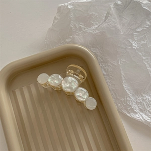 Detail of acrylic hair claw clip with mother-of-pearl beads on a textured tray