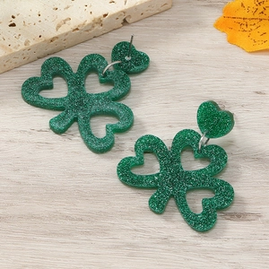 Close-up of green glitter shamrock dangle earrings on a stylish wooden background