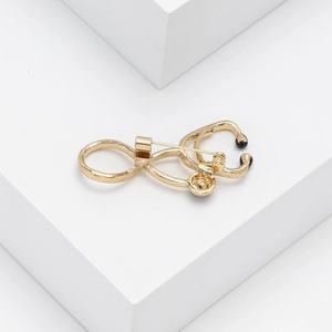 Macro shot of gold-plated stethoscope brooch pin with black earpiece detailing