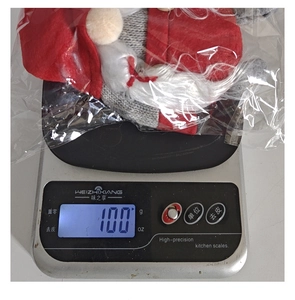 Close-up showing 100g weight of Christmas gnome plush doll on digital scale