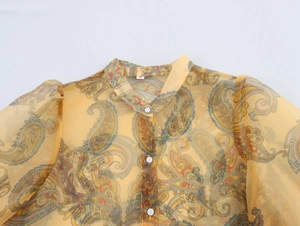 Detail of yellow organza blouse with paisley pattern, puff sleeves and collar buttoning