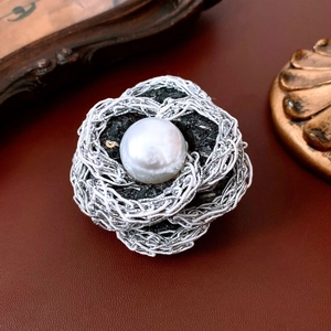 Close-up of pearl camellia brooch with silver woven wire and black tweed fabric