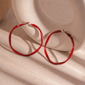 Macro shot of bright red wavy twisted hoop earrings with glossy finish on a ceramic stand