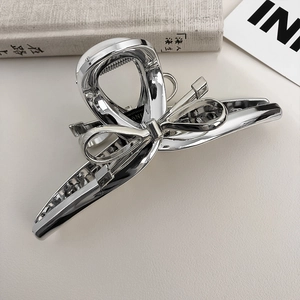 Detail of silver metallic bow hair claw clip on a minimal decorative background