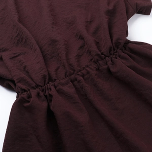 Close-up of the elastic waist detail and wrinkled fabric texture on a dark red romper