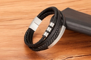 Close-up of men's braided leather bracelet with stainless steel rings on wood background