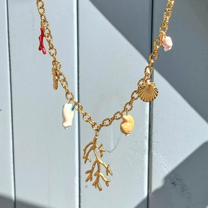 Detail of gold ocean-themed necklace with coral and shell pendants on blue wood