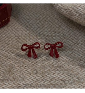 Close-up of deep red bow earrings on beige knit texture with a festive gift box decor