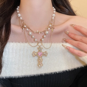 Detail of layered gold cross necklace with pearls and pink heart gemstone on neck