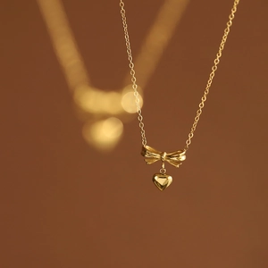 Macro view of gold bow and heart pendant necklace with high-quality polished 18K finish