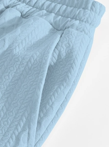 Detail of light blue knit pants showing elastic waistband and geometric texture