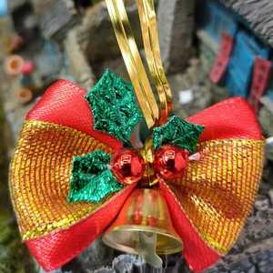 Detail of red and gold striped Christmas bow with green holly leaves and gold bell