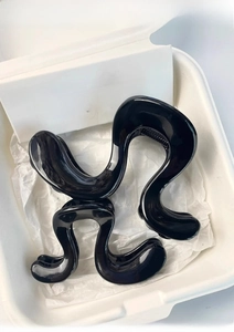 Detail of two glossy black wave hair claws with irregular curved design in a minimalist box