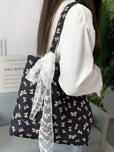 Detail of a black canvas tote with yellow bows and a large white lace bow accent