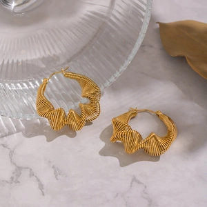 Detail of gold-plated wavy wire-wrapped earrings on a white marble surface